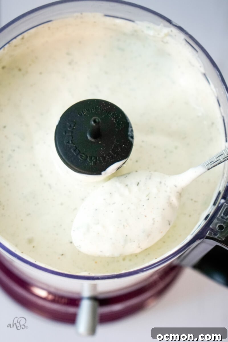 A spoonful of the perfectly blended, creamy green onion dip is being scooped from the food processor, showcasing its smooth texture and rich green color.