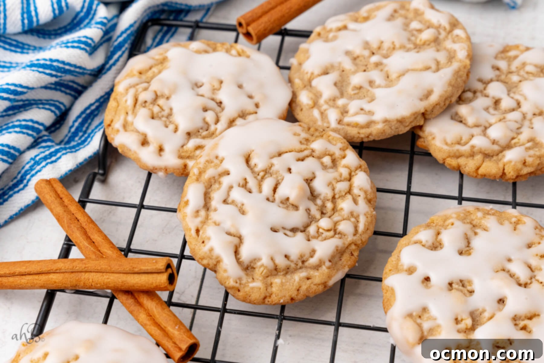 Iced Oatmeal Cookies-17 Five beautifully iced oatmeal cookies are arranged on a wire cooling rack, surrounded by aromatic cinnamon sticks, highlighting their classic appeal.
