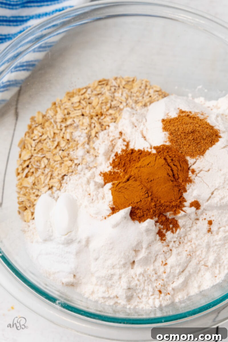 Iced Oatmeal Cookies-2 Various dry ingredients for the cookies, including oats, flour, and spices, are combined in a clear glass bowl, ready for mixing.