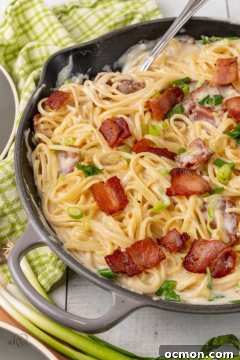 A skillet full of sour cream pasta stirred by a fork and topped with green onions and bacon pieces. 