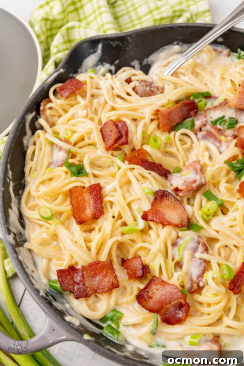 A skillet full of sour cream pasta stirred by a fork and topped with green onions and bacon pieces. 