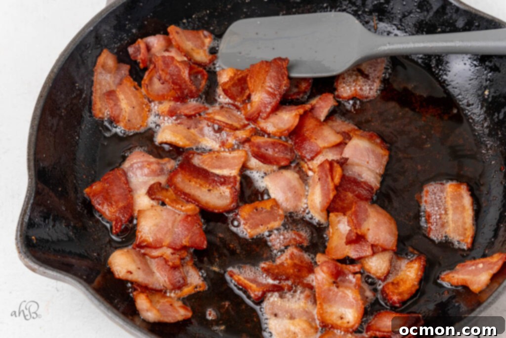 Bacon pieces are cooked in a skillet and stirred with a spatula.