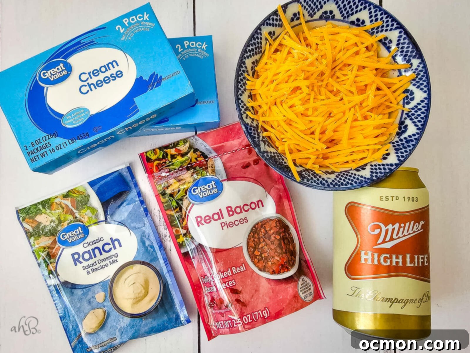 2 packages of cream cheese, a bowl of shredded cheese, a package of Ranch seasoning, a package of Real Bacon Pieces, and a can of Miller High Life are shown