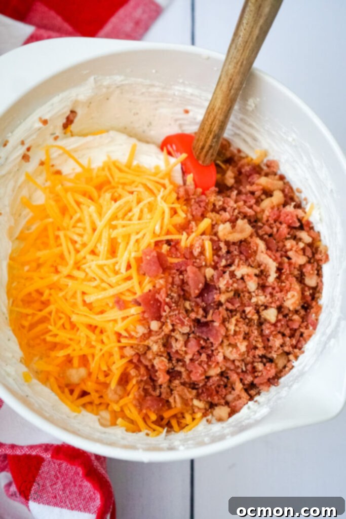 The shredded cheddar cheese and bacon pieces are added to the bowl and mixed in.