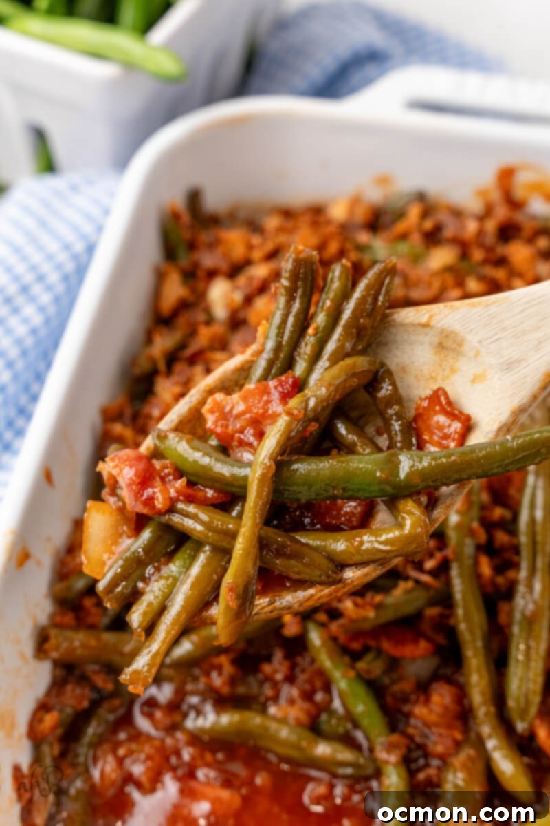 A close-up of a serving of BBQ Green Bean Casserole in a white dish, showcasing the tender green beans, crispy bacon, and golden-brown French fried onions on top.