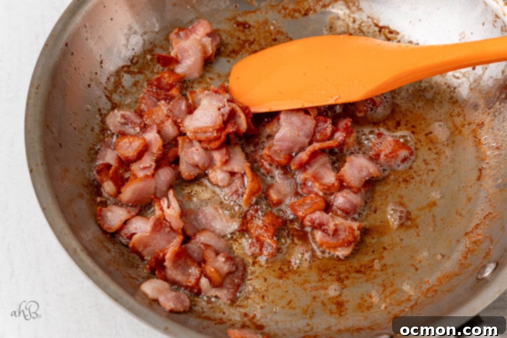Bacon pieces are cooked until crisp in a hot skillet with a spatula.