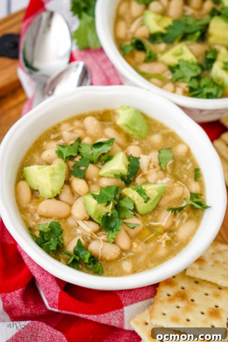 A close-up view of a bowl of creamy 7-Can White Chicken Chili, generously topped with fresh, sliced avocado and bright green cilantro, showcasing its rich texture and inviting appearance.
