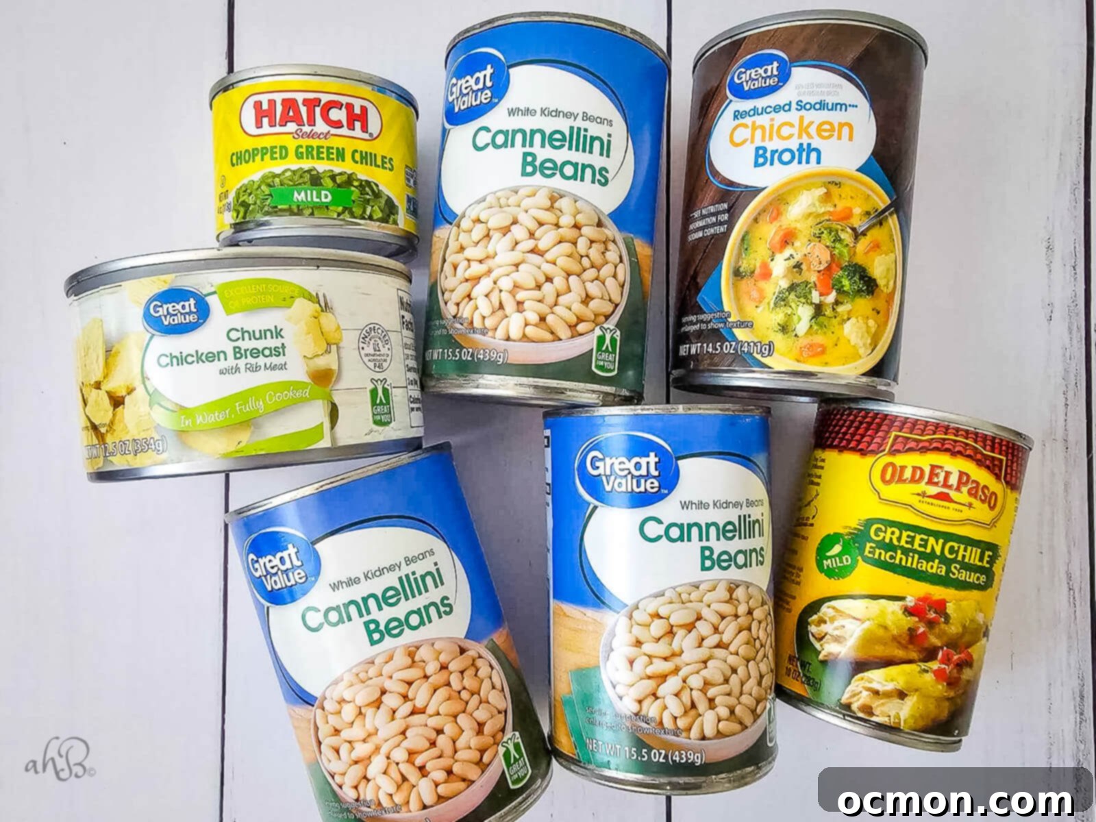 A selection of the key canned ingredients for 7-Can White Chicken Chili laid out: three cans of cannellini beans, one can of chicken broth, one can of chunk chicken breast, one can of chopped green chiles, and one can of green enchilada sauce. These are the building blocks of this easy recipe.