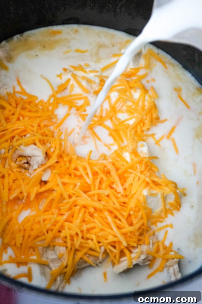 Milk, cubed cream cheese, and shredded cheddar cheese being poured and added to the pot of soup, ready to be stirred until fully melted and creating a wonderfully creamy texture.