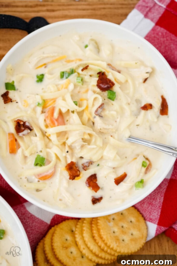 A freshly served bowl of Crack Chicken Noodle Soup, beautifully garnished with a generous amount of crispy bacon pieces, vibrant fresh green chives, and a light sprinkle of shredded cheese, inviting you to enjoy.
