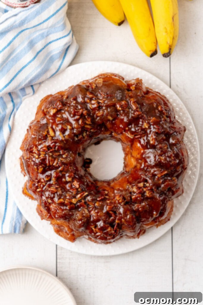 The freshly baked Bananas Foster Monkey Bread is inverted onto a white serving plate, gleaming with sticky sauce.
