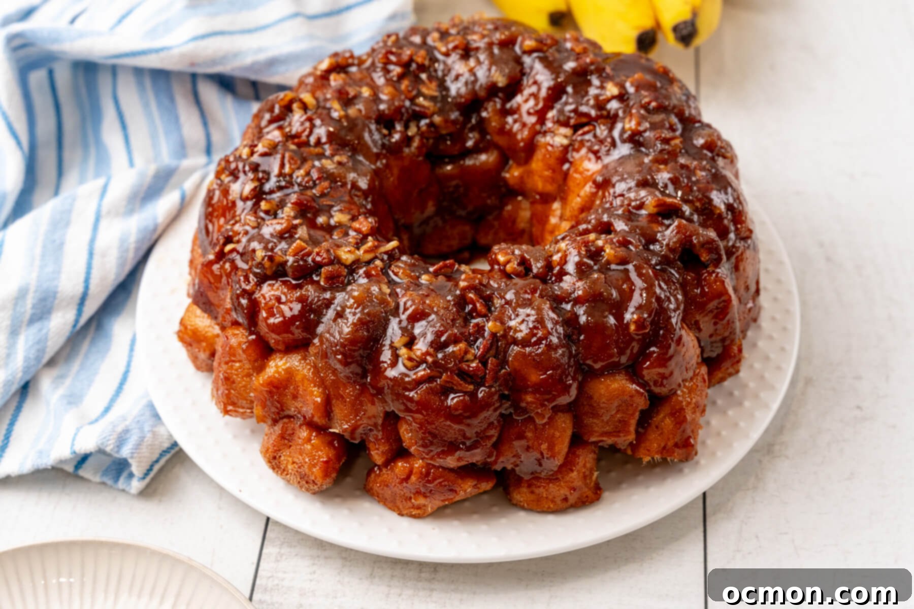 A beautiful Bananas Foster Monkey Bread on a white plate, glistening with its rich, sticky rum sauce.