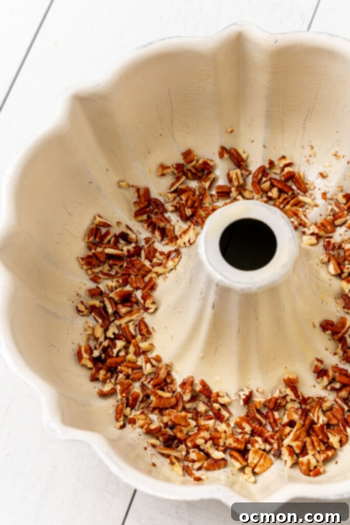 Chopped pecans are evenly spread across the bottom of a greased Bundt pan.