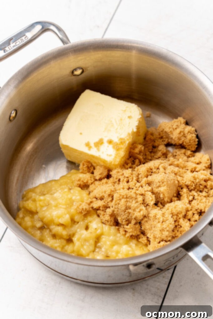 Butter, brown sugar, and mashed ripe bananas are being added to a saucepan on the stovetop.