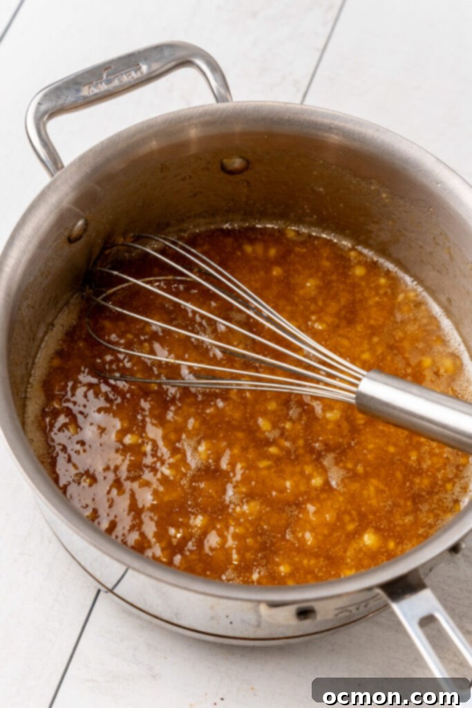The golden banana caramel mixture is removed from the heat, with a whisk resting in the pan.