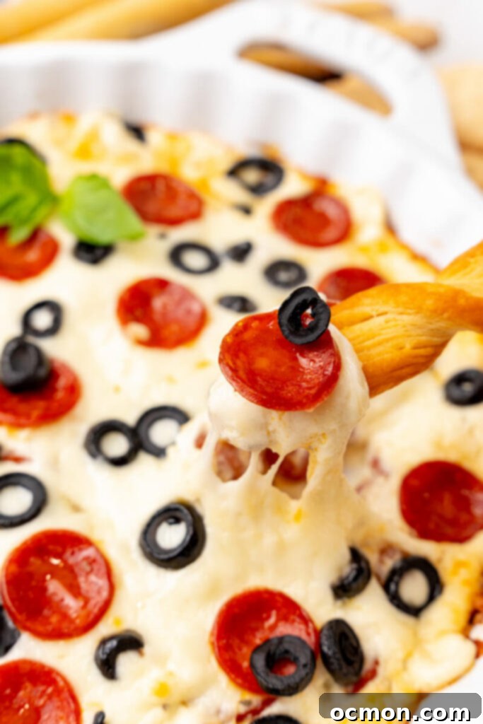 A breadstick scoops up hot, melted cheesy pepperoni dip, revealing gooey cheese and savory pepperoni pieces.
