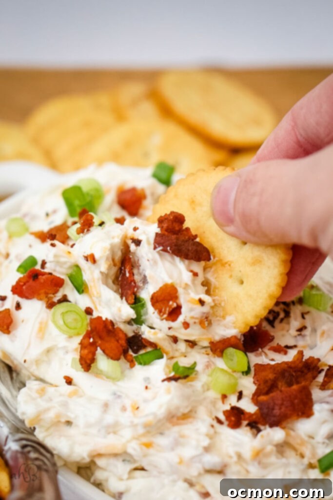 A close-up of a bowl of creamy Ranch Beer Cheese Dip, garnished with chives and served with pretzels.