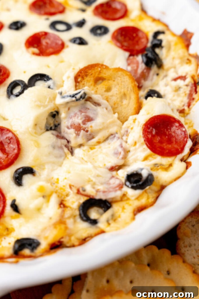 A toasted round, laden with hot, melted pepperoni dip, is lifted from a pie plate, ready for a delicious bite.