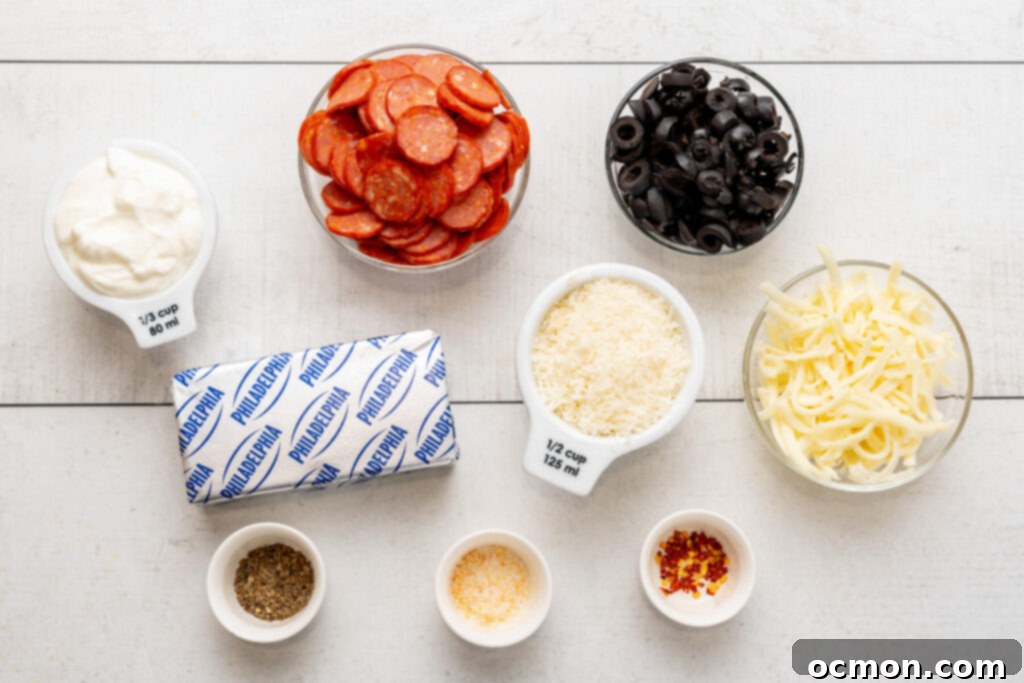 A collection of fresh ingredients laid out for making pepperoni dip: sour cream, pepperoni slices, black olives, cream cheese, shredded Parmesan cheese, shredded mozzarella cheese, Italian seasoning, garlic salt, and crushed red pepper flakes.