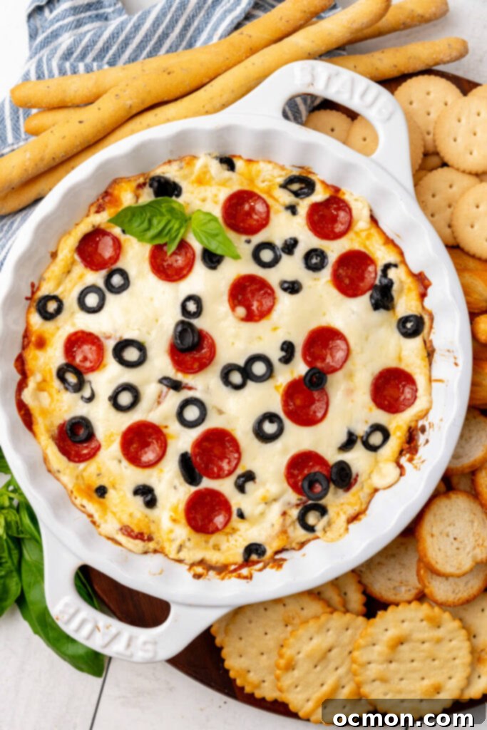 A baked pie plate of hot pepperoni dip sits alongside a serving tray of assorted crackers and dippers, ready for a party.