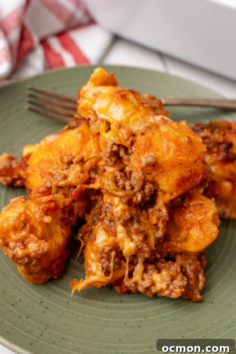 A generous serving of bubbly and cheesy Sloppy Joe Biscuit Casserole on a vibrant green plate, showcasing the golden-brown biscuits and rich filling.