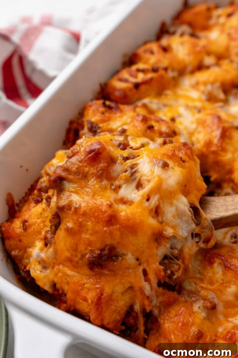 A wooden spoon scooping out a generous portion of warm and bubbly Sloppy Joe Biscuit Casserole from a casserole dish, showing the texture of the biscuits and meat.