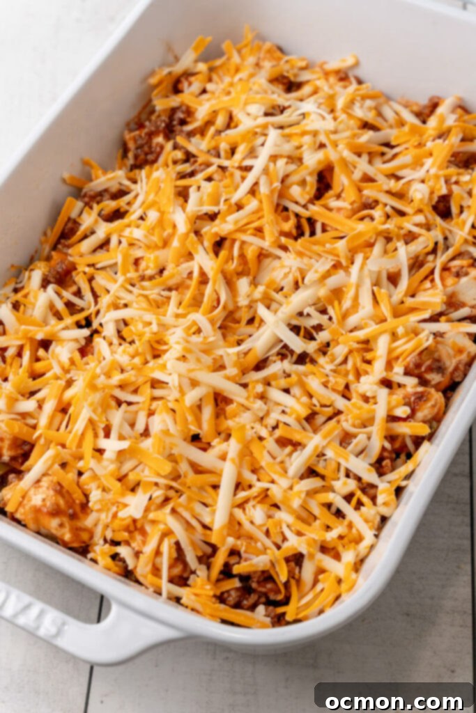 The sloppy joe meat and biscuit mixture being spread evenly into a 9x13 inch casserole dish, then topped with the remaining shredded cheese.