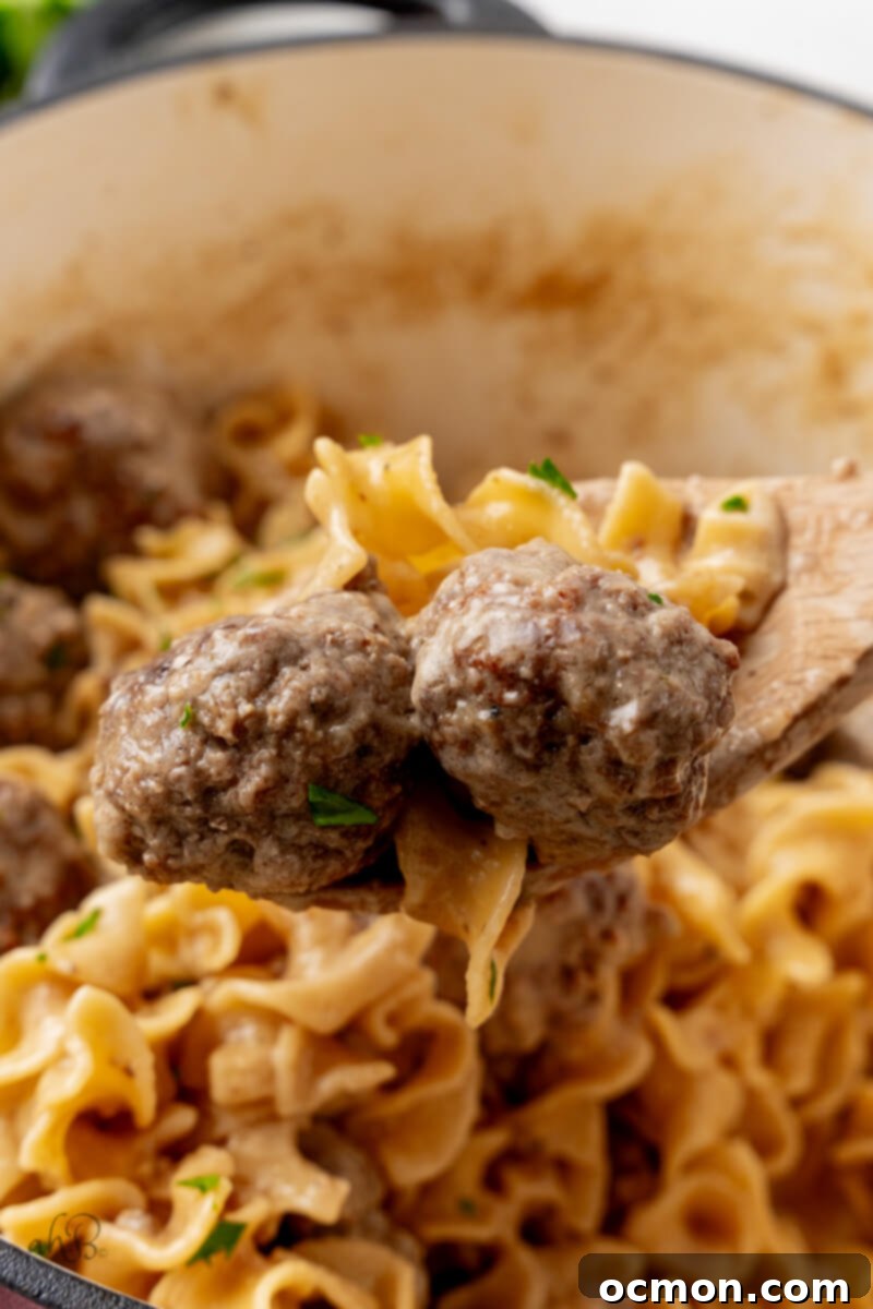 Two Swedish meatballs held by a wooden spoon over the pot, showing their perfectly browned exterior.