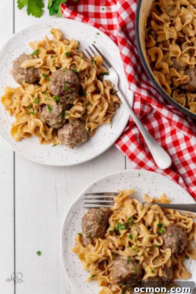 Two plates of Swedish meatballs and noodles are served, garnished with fresh herbs and a side of green vegetables.