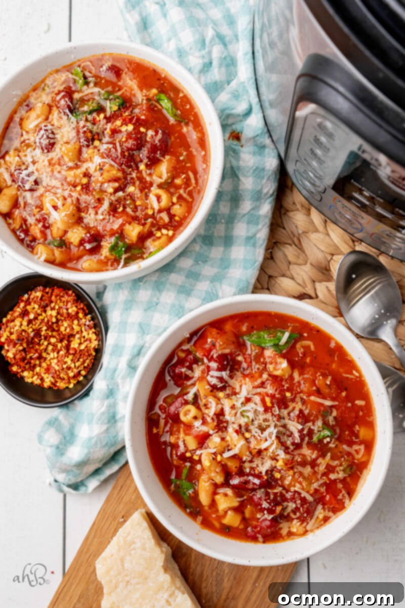 Two white bowls of Instant Pot Minestrone Soup, garnished with Parmesan and red pepper flakes, with the Instant Pot in the background.