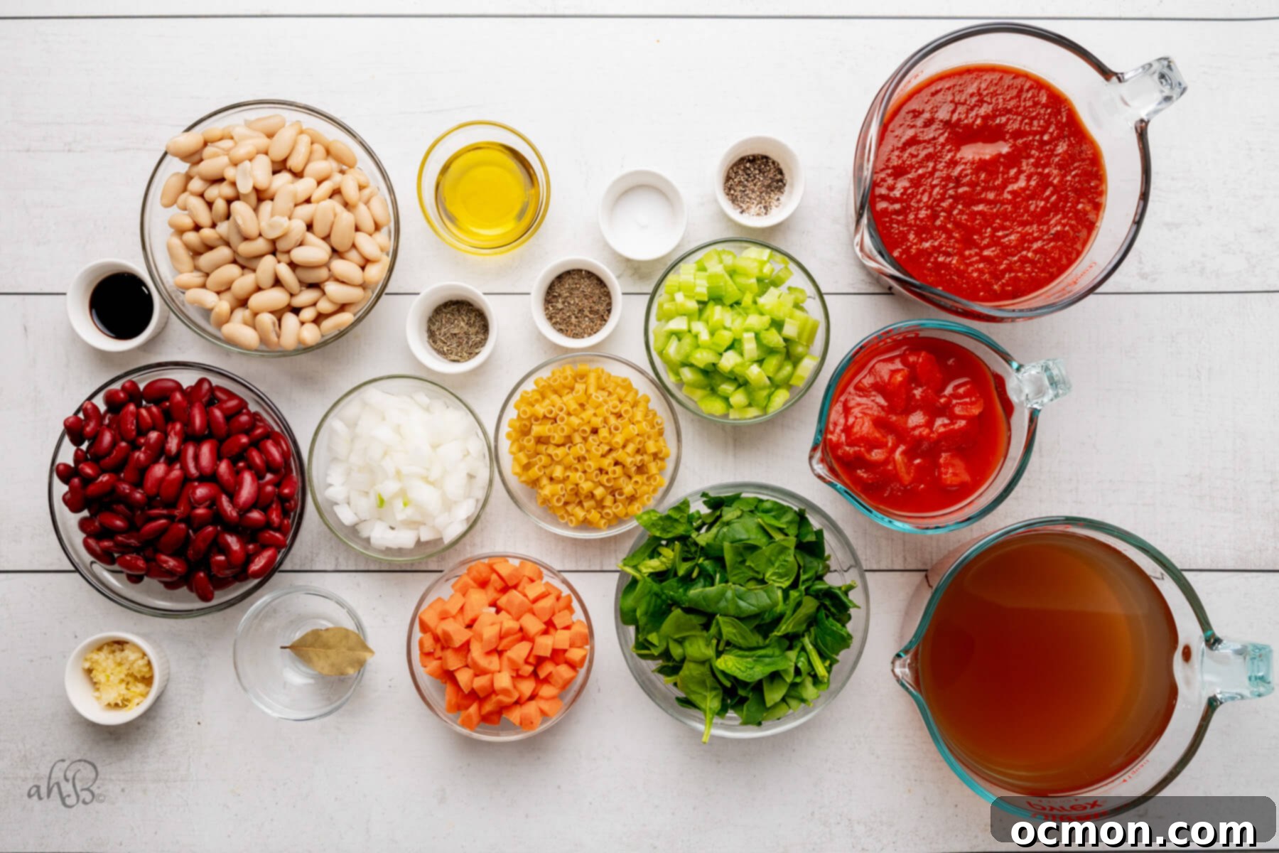 Various fresh ingredients for Minestrone soup, including vegetables, canned goods, and pasta, arranged in glass bowls.