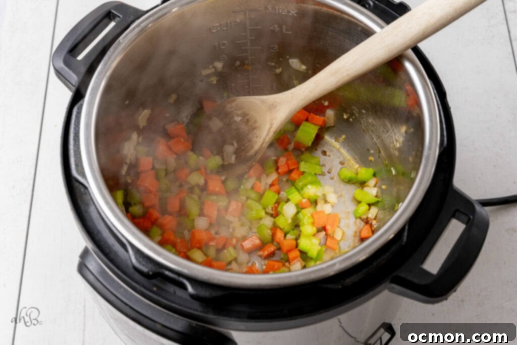 Chopped celery, carrots, onion, and minced garlic are sautéed in olive oil within the Instant Pot liner.