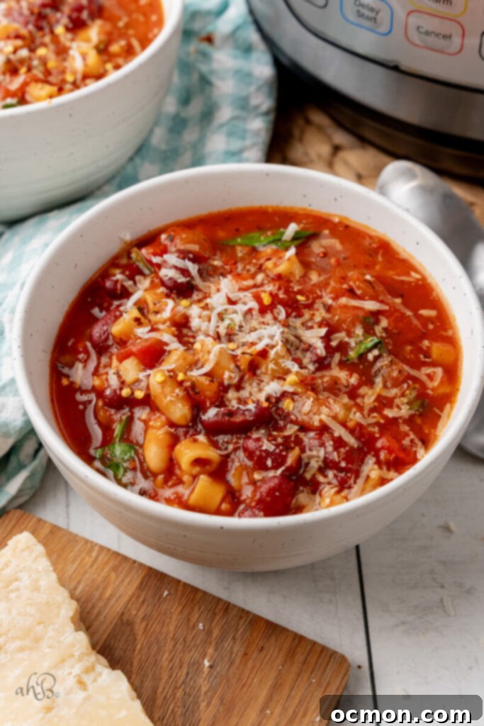 A beautifully garnished white bowl of Minestrone Soup with Parmesan cheese and chili flakes.