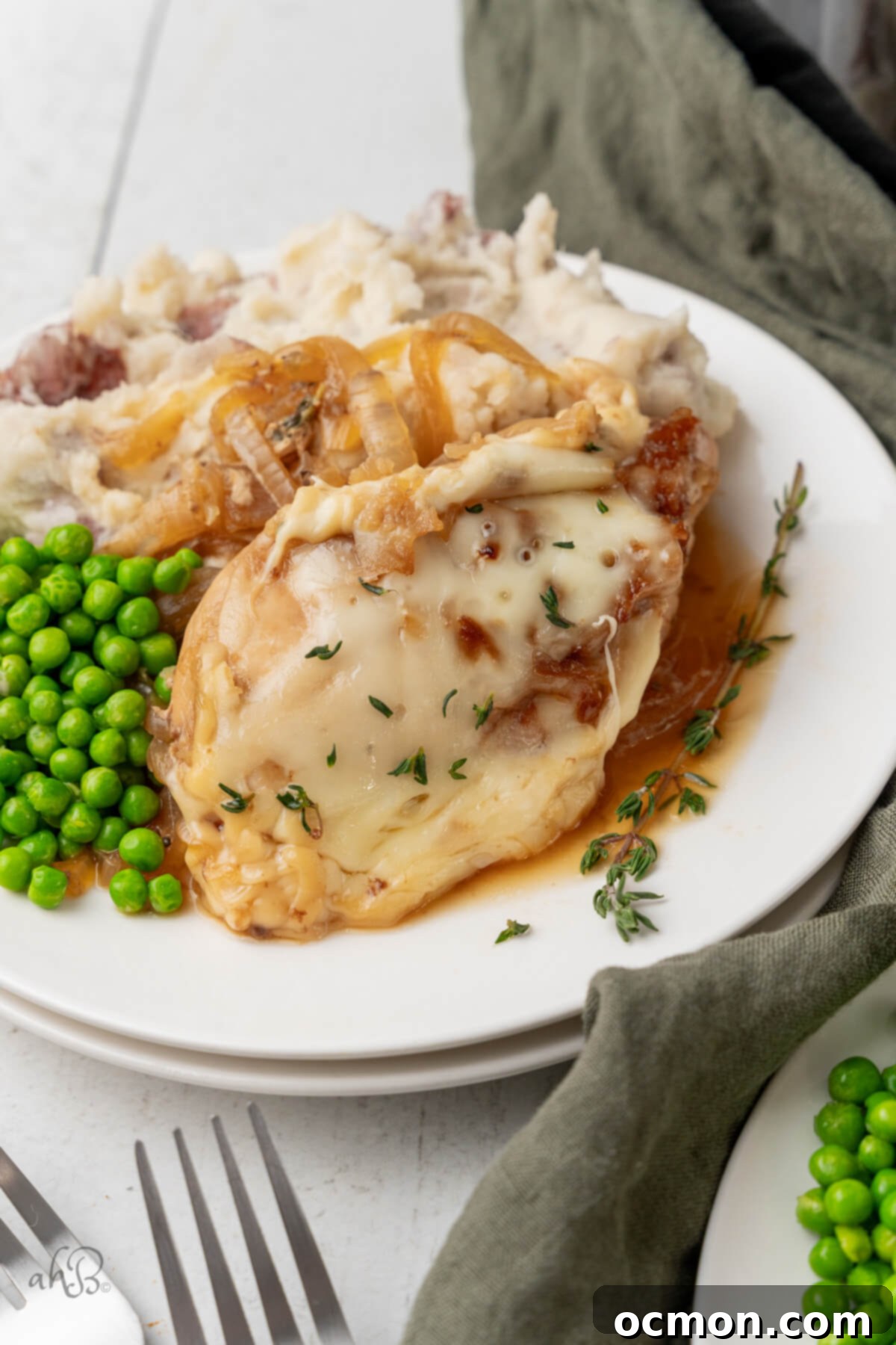 Easy Slow Cooker French Onion Chicken 2 A serving of French Onion Chicken with peas and mashed potatoes on a white plate.