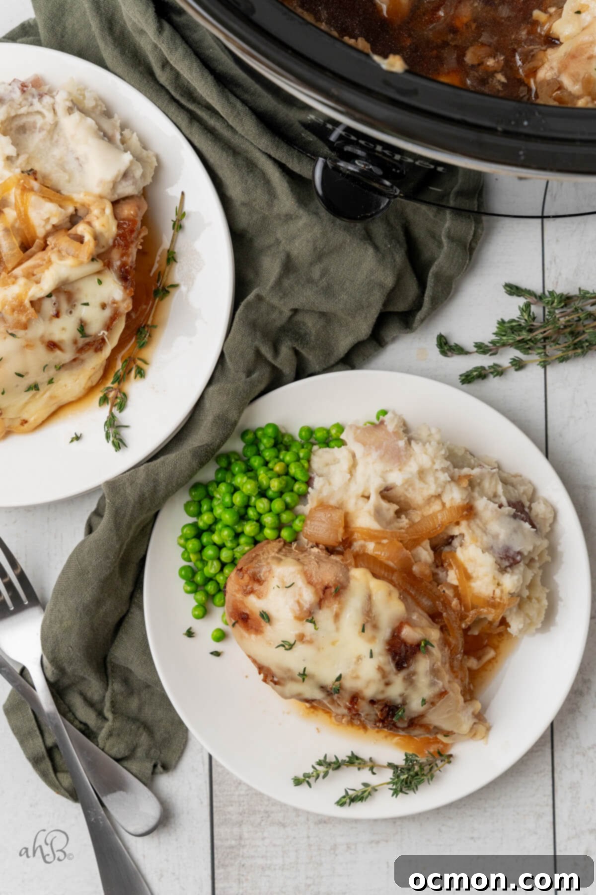 Easy Slow Cooker French Onion Chicken 3 Two plates of French Onion chicken, mashed potatoes, and peas, served on white plates next to the crockpot.