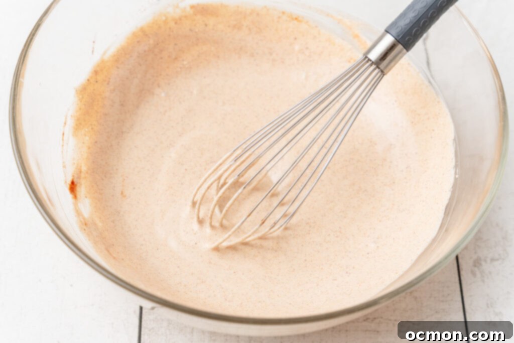 The ingredients for the creamy dressing are mixed together in a bowl with a whisk, showing the smooth, orange-hued mixture.