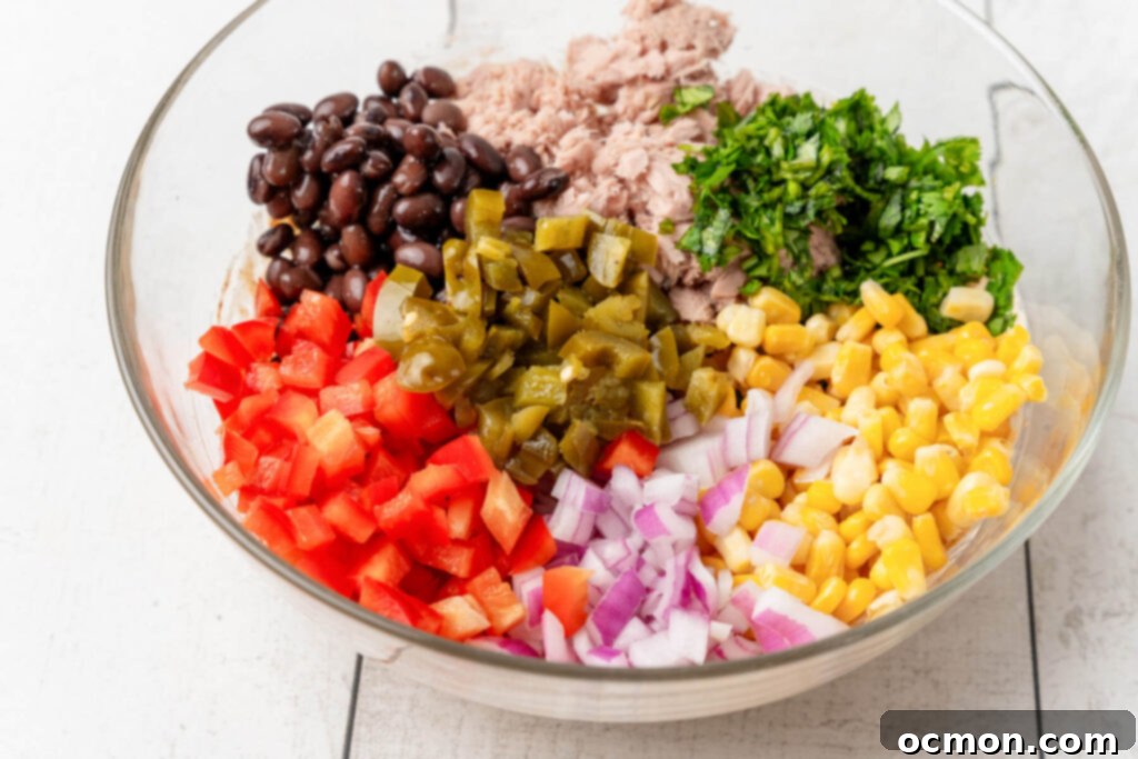 Drained tuna, corn, black beans, red onion, red bell pepper, pickled jalapeño, and chopped cilantro are added to a large mixing bowl, ready to be combined with the dressing.