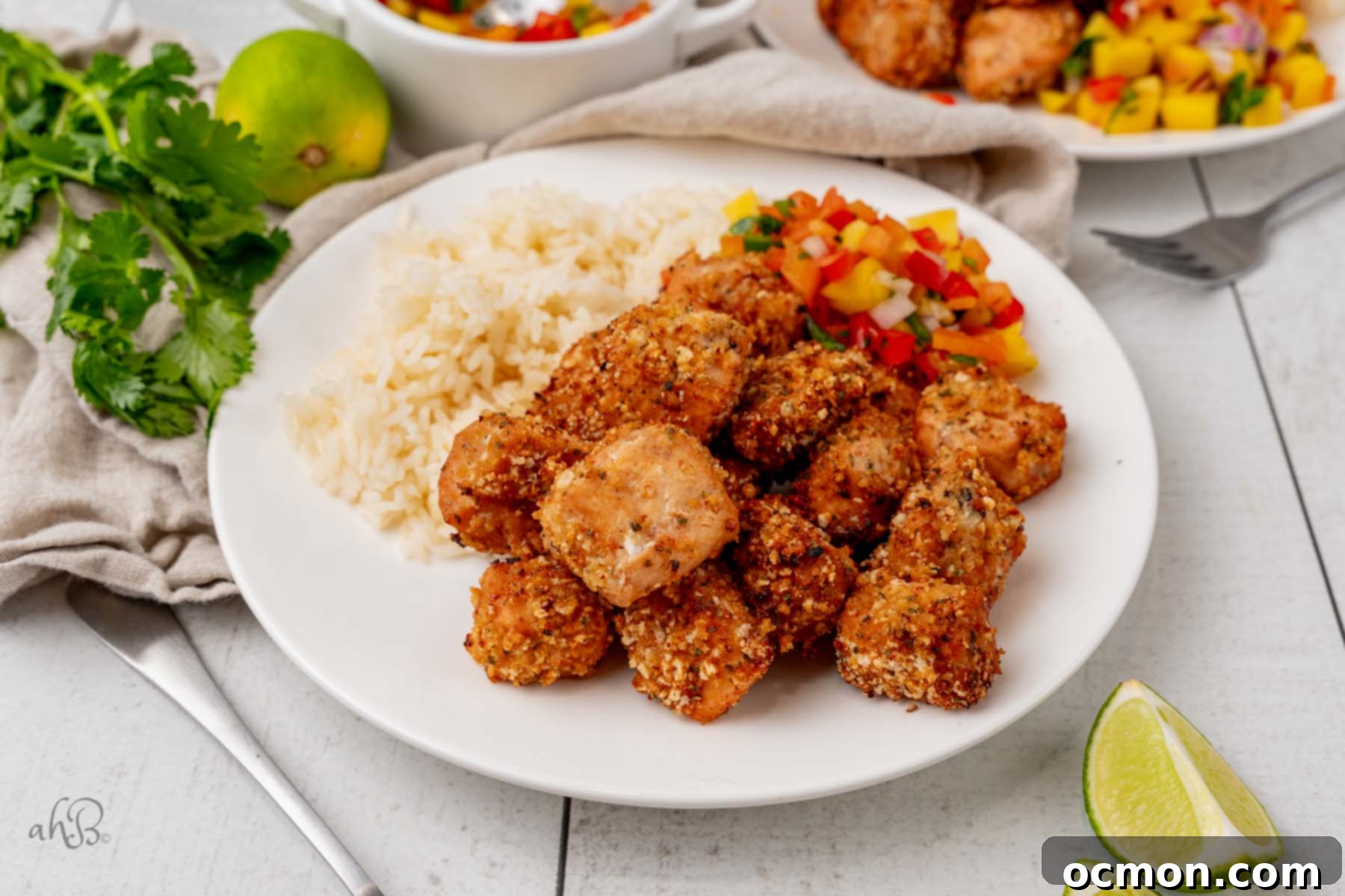 A beautifully presented white plate showcasing a generous serving of golden-brown air fryer salmon bites, accompanied by fluffy rice and a vibrant, fresh mango salsa blend, ready for a delicious meal.