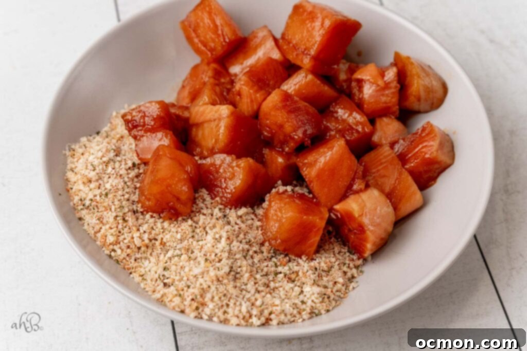 Marinated salmon cubes are carefully being tossed and coated evenly in the savory breadcrumb and spice mixture, ensuring a complete and crispy crust forms on each delicious piece.