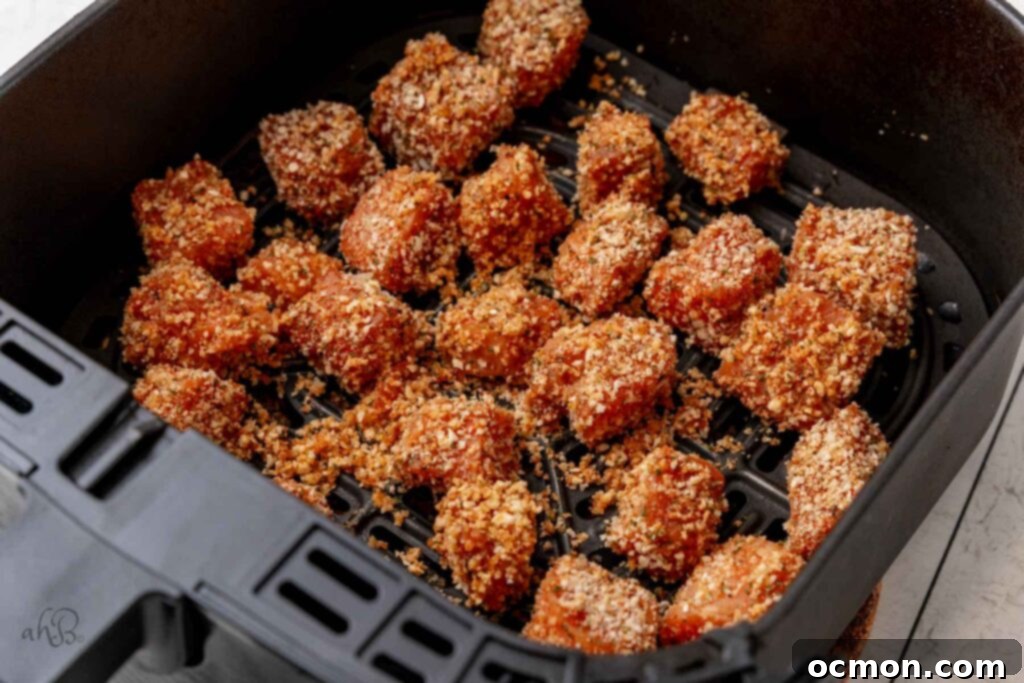 The breaded salmon bites are meticulously arranged in a single layer inside the air fryer basket, showing ample space between each piece to ensure even cooking and maximum crispiness.