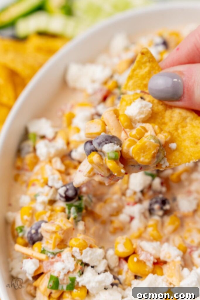 A golden tortilla chip expertly loaded with a generous scoop of vibrant Fiesta corn dip, ready for a delightful bite. 