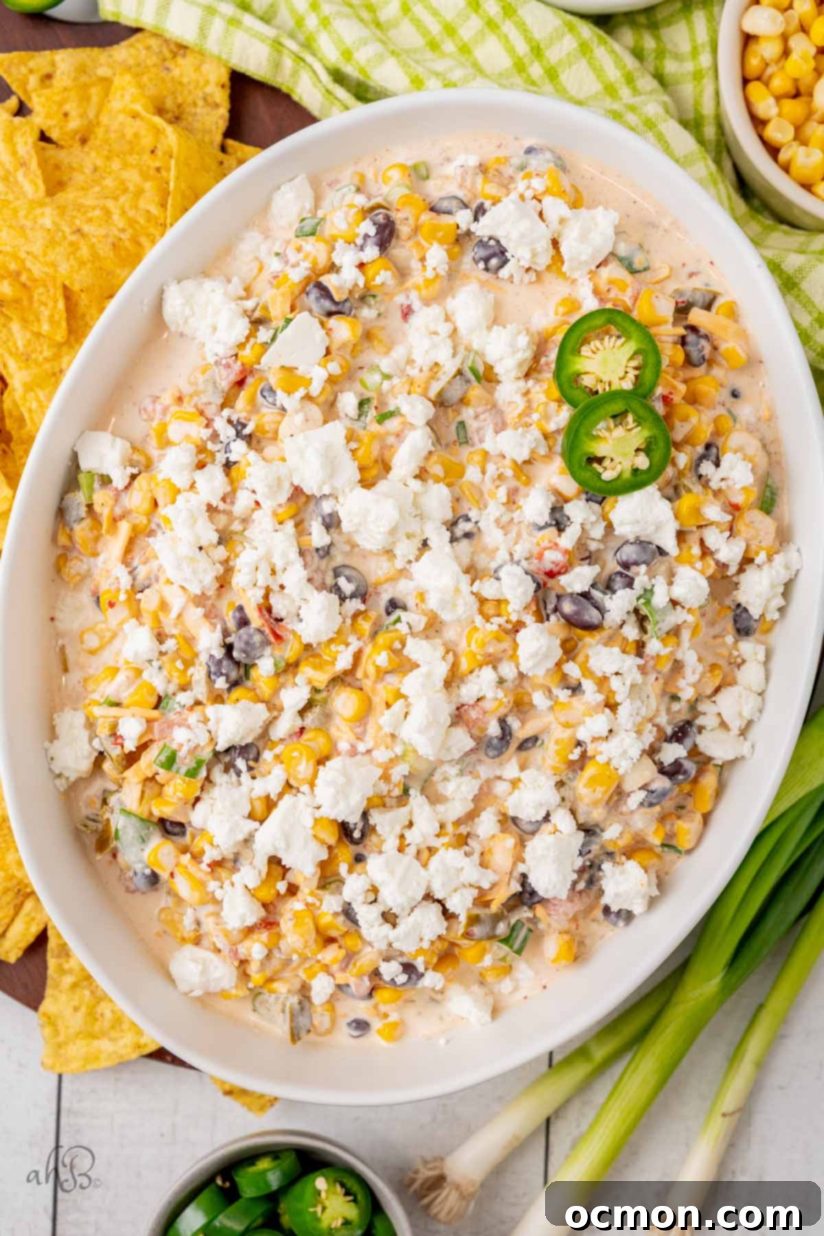 Fiesta Corn Dip in a white bowl, topped with cheese and jalapeños.