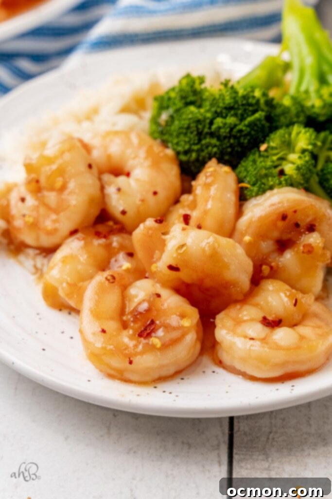 A white plate with a serving of sticky honey garlic shrimp and steamed broccoli to one side. 
