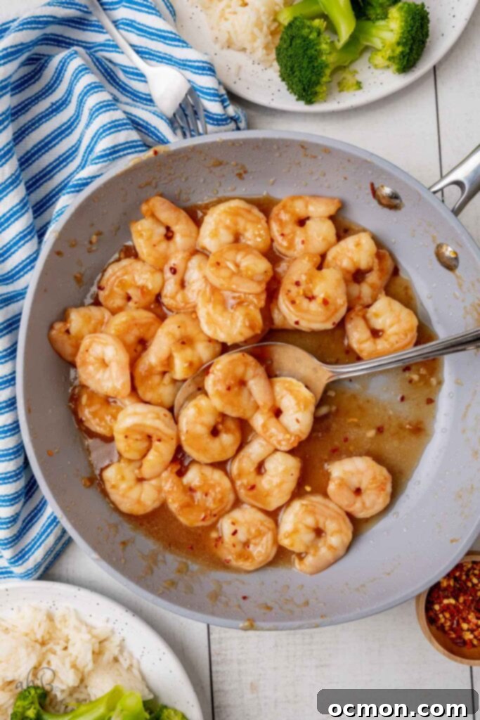 A gray nonstick skillet full of sticky honey garlic honey shrimp. 3 shrimp rest in a spoon. 