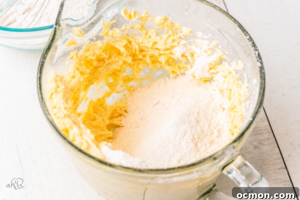Orange Zest Chocolate Shortbread 7 The pre-measured flour is carefully added to the creamed butter and sugar mixture in a glass mixing bowl, signaling the next stage of dough preparation.