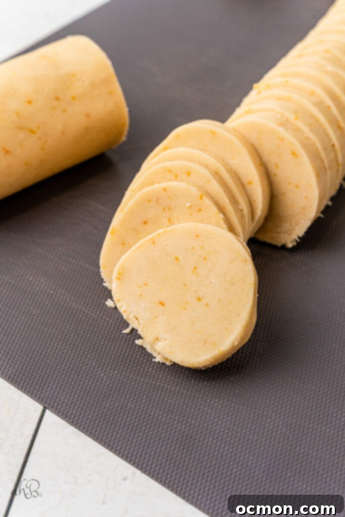 Orange Zest Chocolate Shortbread 10 A chilled log of shortbread dough being precisely cut into uniform slices on a cutting board, ready for baking into perfect cookies.
