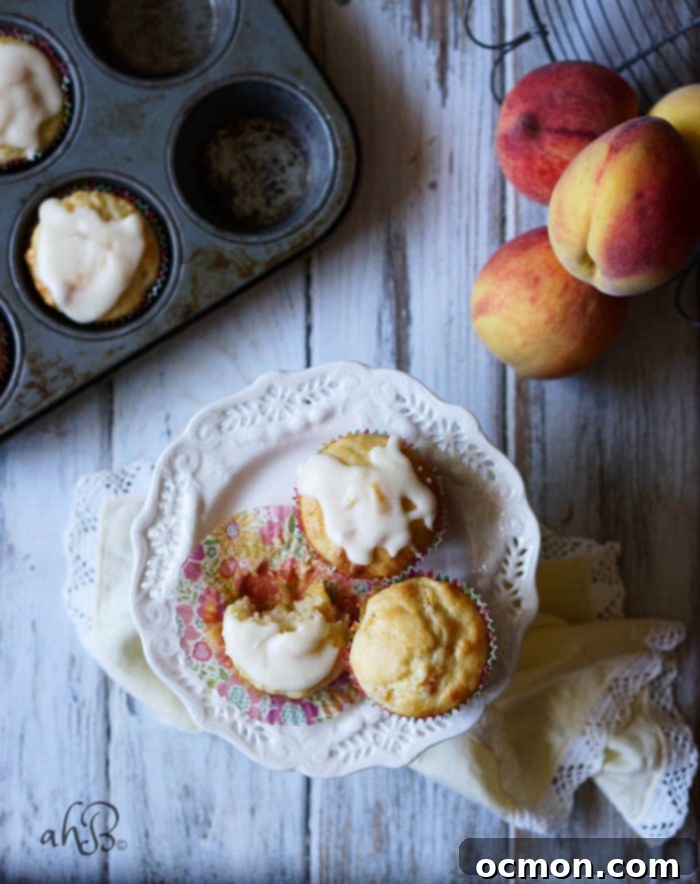 Golden Peach Cloud Muffins 5 A close-up of a Peaches and Cream Muffin, showing its soft, moist interior and generous chunks of baked peach, beautifully adorned with a delicate vanilla glaze