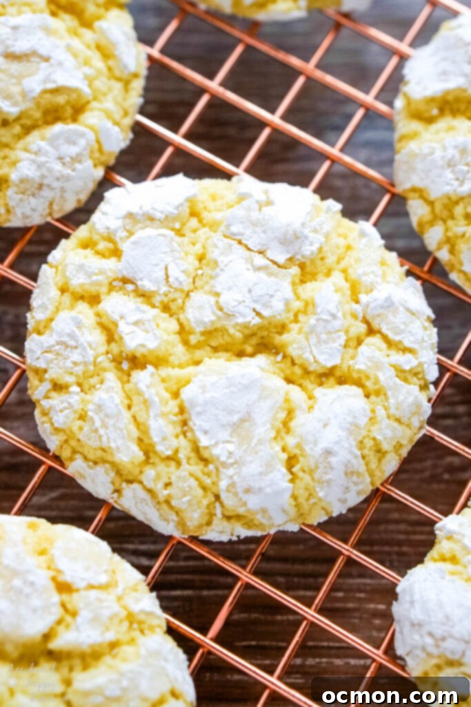 A close-up image showcasing the perfectly cracked, powdered sugar-dusted surface of a baked lemon crinkle cookie, revealing its soft, lemony interior.