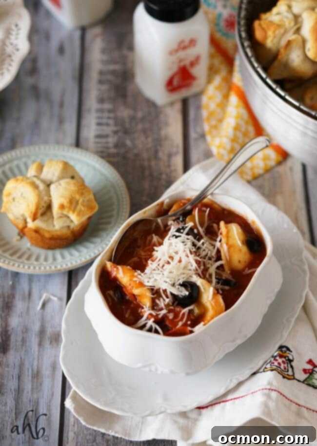 Close-up of a bowl of pepperoni pizza soup, showing mini pepperonis, melted mozzarella, and black olives