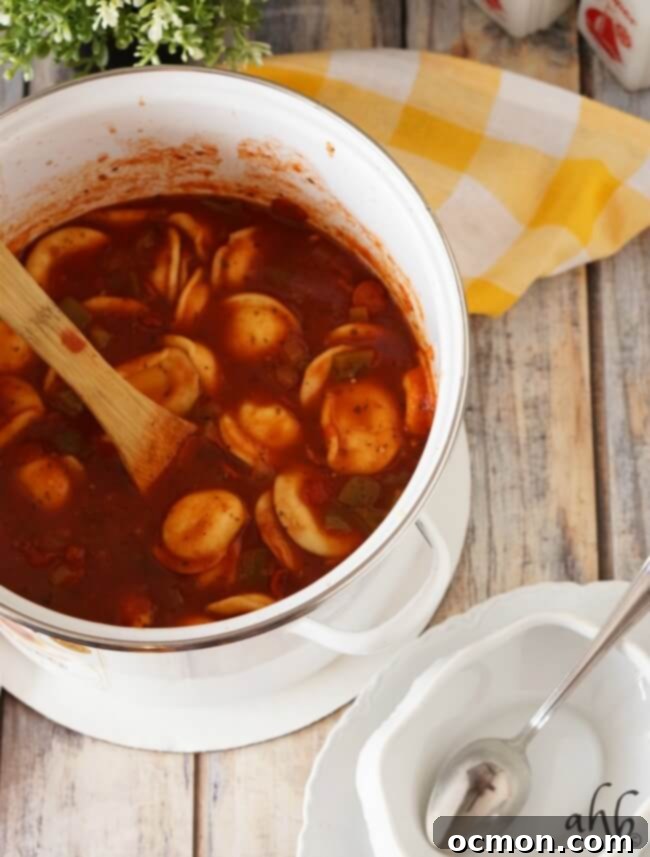 Pepperoni pizza soup bubbling in a large pot, with ingredients like tomatoes, pepperoni, and ravioli visible
